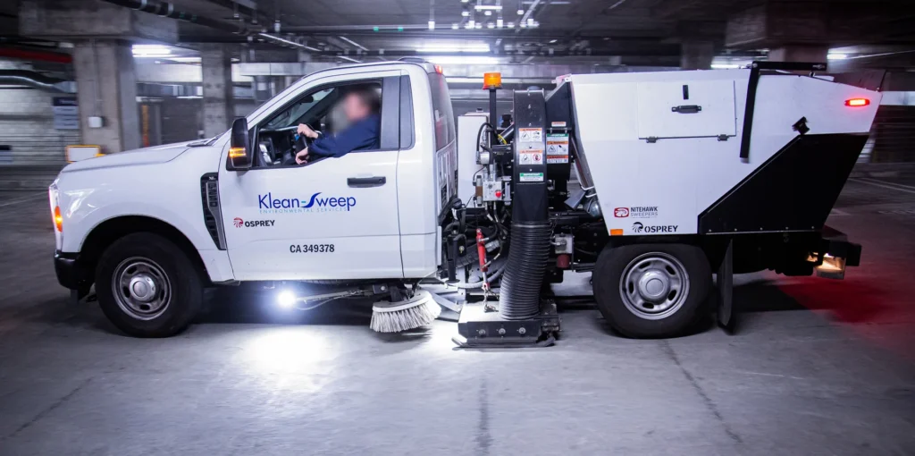 Operator in blue uniform performing a pre-trip inspection on a street sweeper